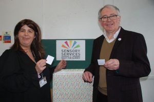 Image shows Clare Burgess, new CEO of Sight for Surrey holding a winning Centenary Raffle ticket in her hand. Next to her is a large box filled with raffle tickets. The other side of the box is retiring CE, Bob Hughes also holding a winning raffle ticket.
