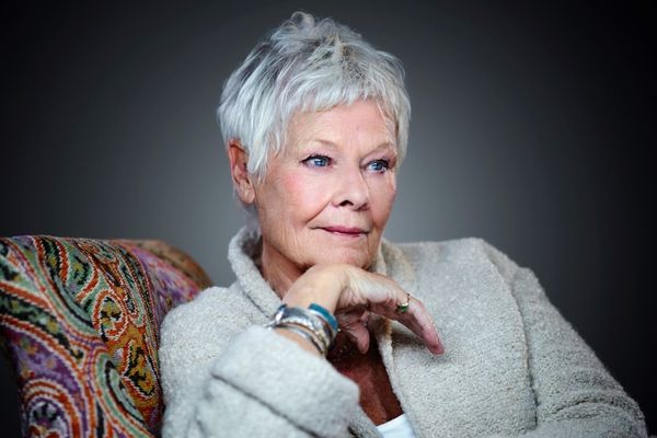 Dame Judi smiling looking slightly off camera with her chin resting on her hand.