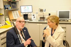 The Duchess is sat talking to a service user in the Resource Centre surrounded by lots of helpful sight and hearing loss equipment.