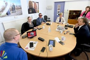 A group of people sat round a table with various pieces of tech equipment laid out on the table.