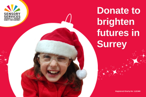 Image shows a young girl laughing at the camera, she is wearing a Santa hat and a red coat, she is surrounded by a bauble shape. The words 'Donate to brighten futures in Surrey' sit to her right in bold
