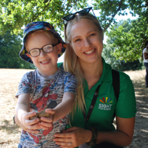 Trainee Habilitation Specialist Sharn with a small child our charity have supported within the Children and Young People's Services team. They are in a sunny park.