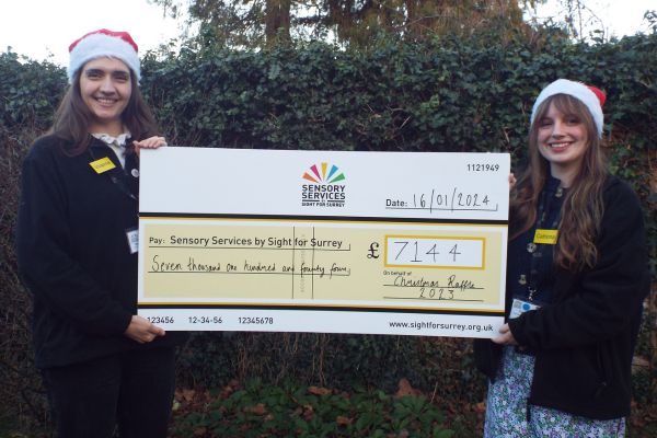 Image shows Vivienne and Catriona holding a large cheque made payable to Sensory Services by Sight for Surrey showing the amount of £7,144.