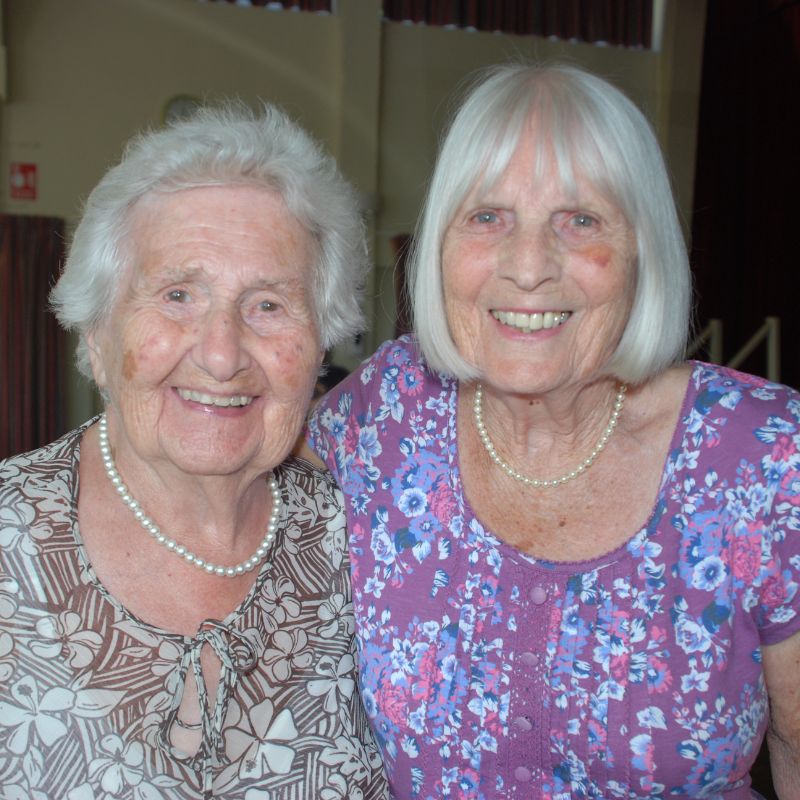 Two ladies standing shoulder to shoulder both smiling at the camera