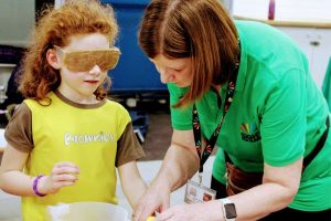 Image description: a member of staff from the charity supporting a child in a Brownie top wearing simi specs.