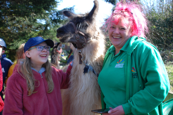 Image description: a young person we support is standing and stroking a llama with Fi, our Children and Young People’s Team Activities Coordinator. All are smiling at the camera.