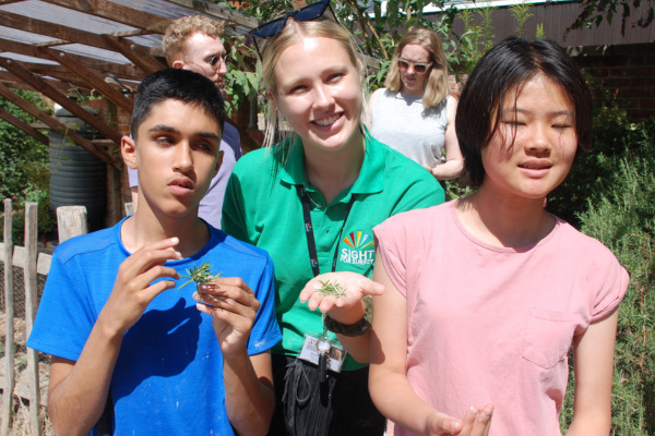 Image shows a member of staff with two young people supported by the charity, they are showing herbs in their hands that they have picked from the garden.