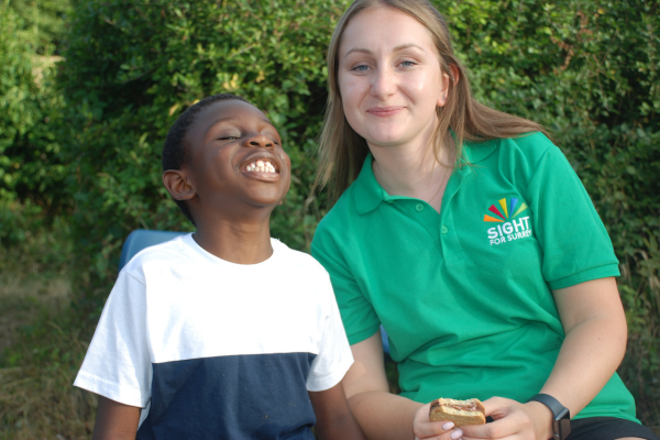 Image shows a member of staff from the charity sitting next to a young boy who is tilting his head upwards, he has a beaming smile.