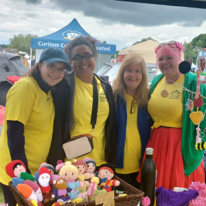Image shows four ladies from the charity at our stall, a basket of cute crochet toys made by staff is on the table in front of them.