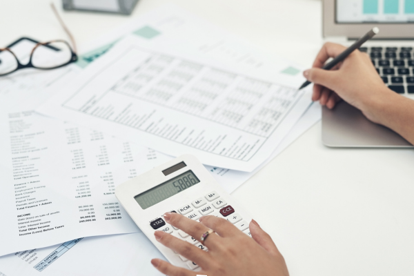 Image shows a piece of paper on a desk surrounded by a calculator, pen and pair of glasses.