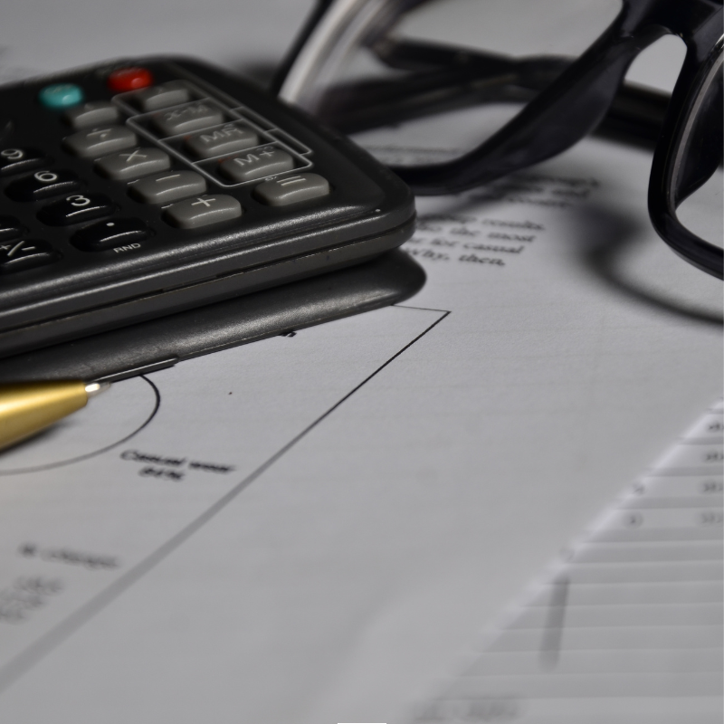 Image shows a piece of paper on a desk surrounded by a calculator, pen and pair of glasses.