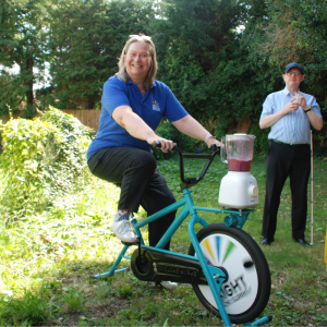 Image shows Cathy Long, ECLO pedaling on our smoothie bike, blending her own delicious smoothie.