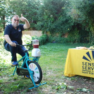 Image shows Joe Collins, Deaf Services Team, pedalling on our smoothie bike making his own delicious smoothie.