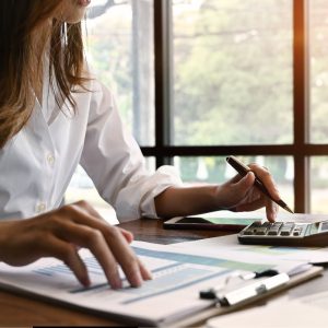 Image shows a person sitting at a desk with a calculator and pen and they are working off a clipboard.