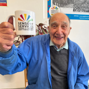 Image shows Reg an attendee to Meet Up Catch Up smiling at the camera, he is holding up a mug and looks very happy.