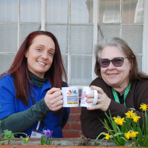 Image shows Natalie from the Community Engagement team with a lady attending Meet Up Catch up they are both holding mugs.