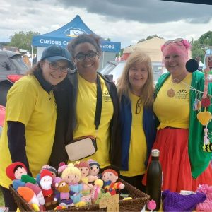 A group of women are standing shoulder to shoulder behind a table laden with items at Ashtead Village Day.