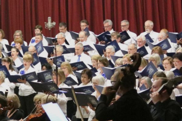 The New Egham Singers performing at an event they all dressed in white shirts and holding a book of lyrics in their hands.