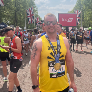 Darren at the end of the London Marathon 2025 he is wearing a yellow Sensory Services by Sight for Surrey vest and has his medal around his neck.