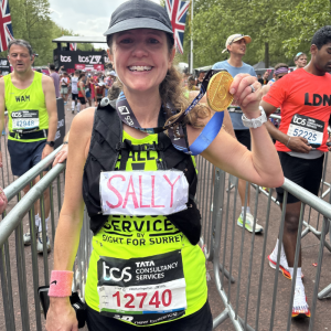 Sally has completed the London Marathon 2025 she is over the finish line and has a medal round her neck and smiling at the camera