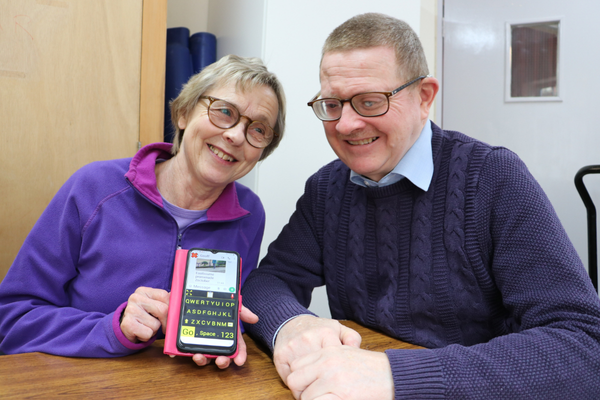Gary, Tech Trainer is supporting a woman with using the accessibility features on her iPhone. The woman is smiling at the camera and holding her iPhone.
