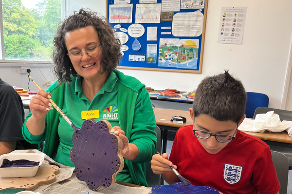 A member of staff from the CYPS Team is sitting at a table painting with a young boy we support.