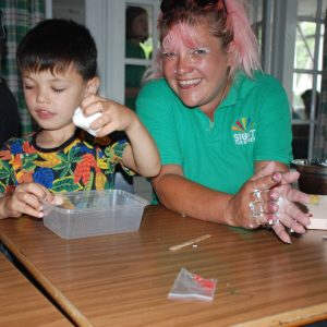 A member of staff from the charity is supporting a young boy making slime.