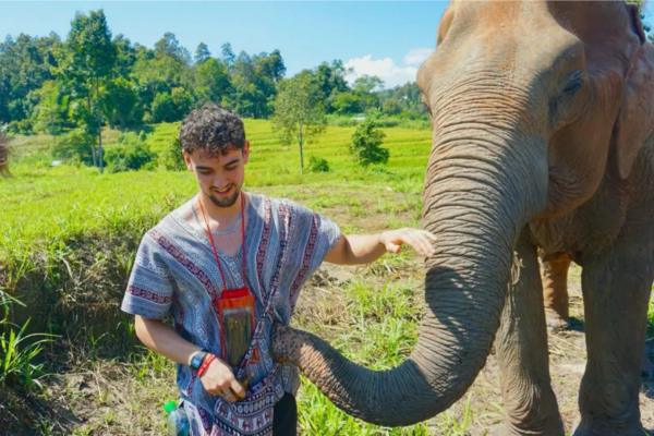 Calum has his head slightly bent and is standing next to an elephant