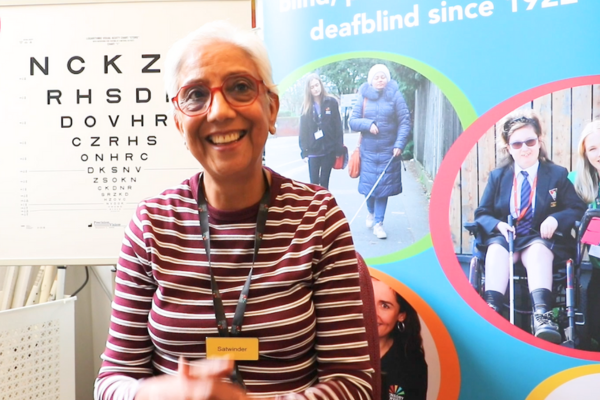 A smiling Satwinder is sitting infront a eye test chart