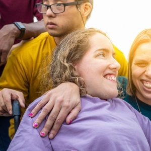 Two disabled women are standing next to each other and a disabled man is standing behind them. 