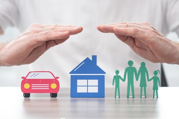 Cuts out of a car, house and people with a person standing behind protecting the cut outs with their hands