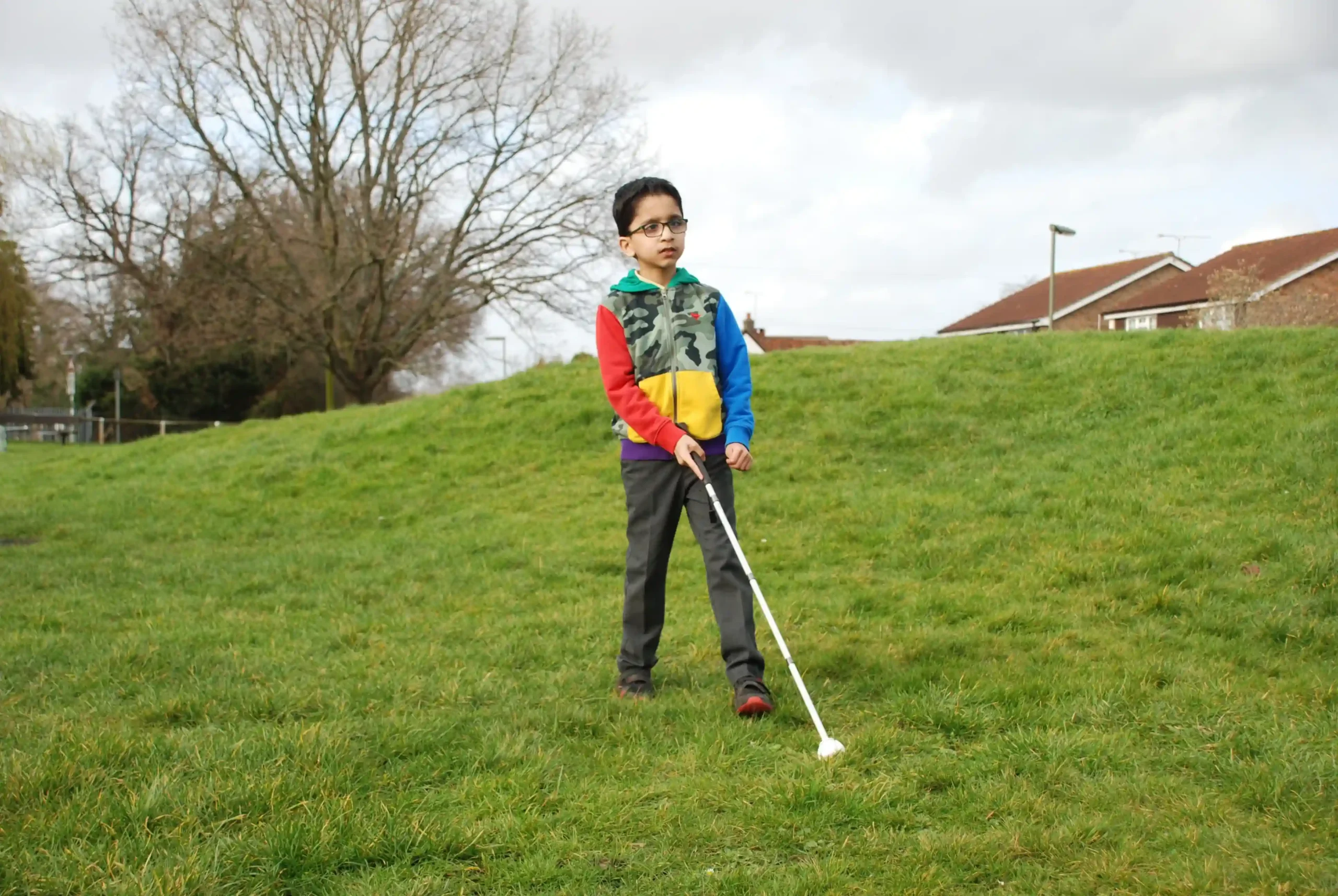 A young boy with a cane walking across grass.