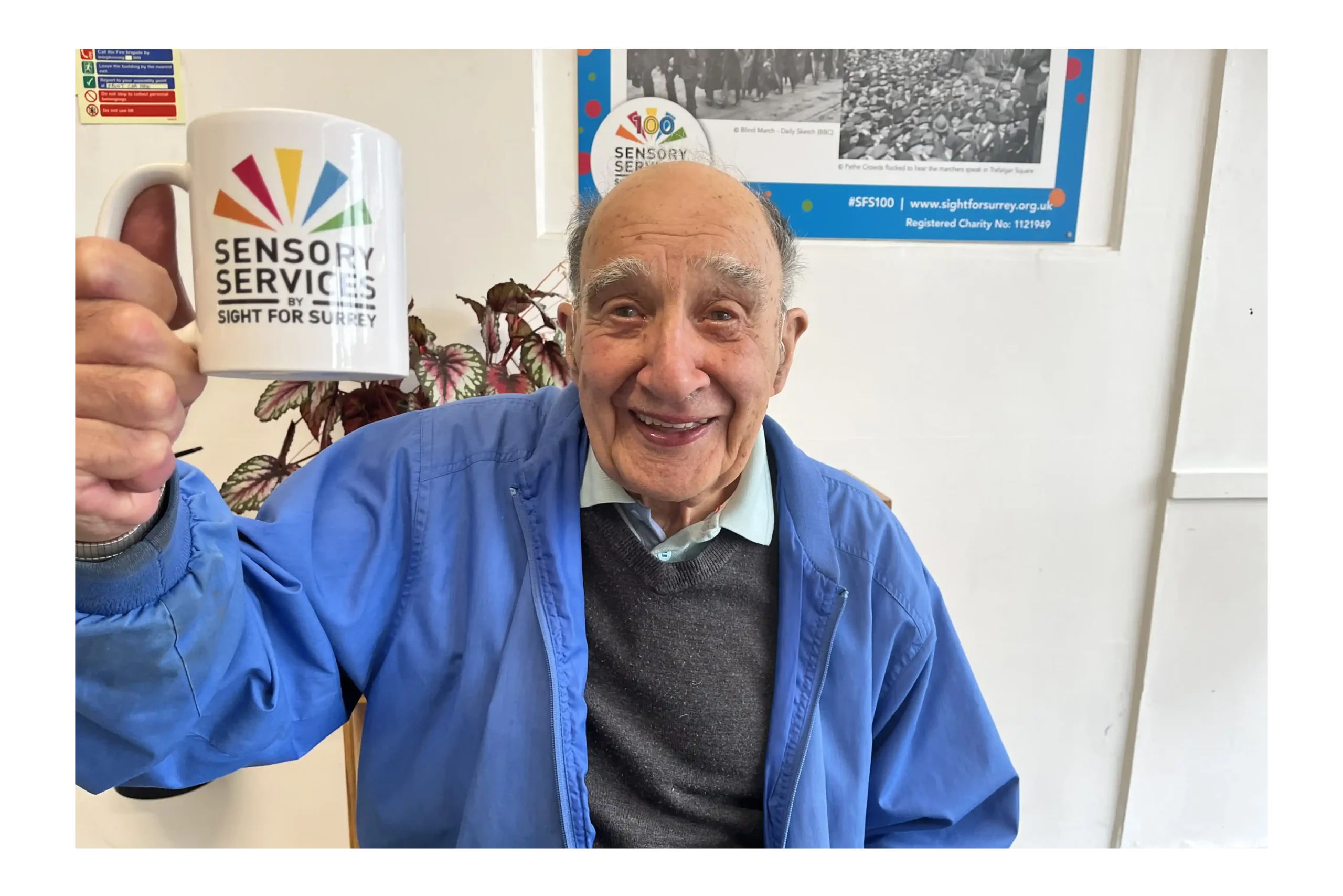 An elderly man supported by the charity holding a branded branded up in the air, he is smiling.