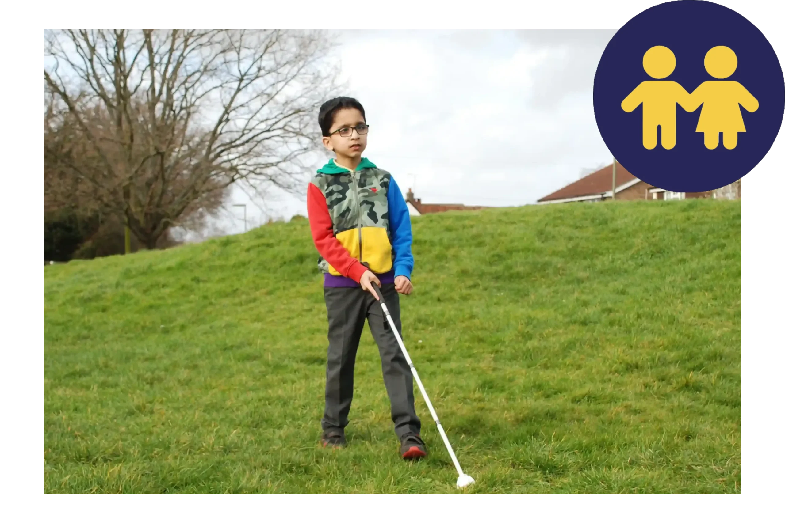 A young boy with a cane walking over grass.