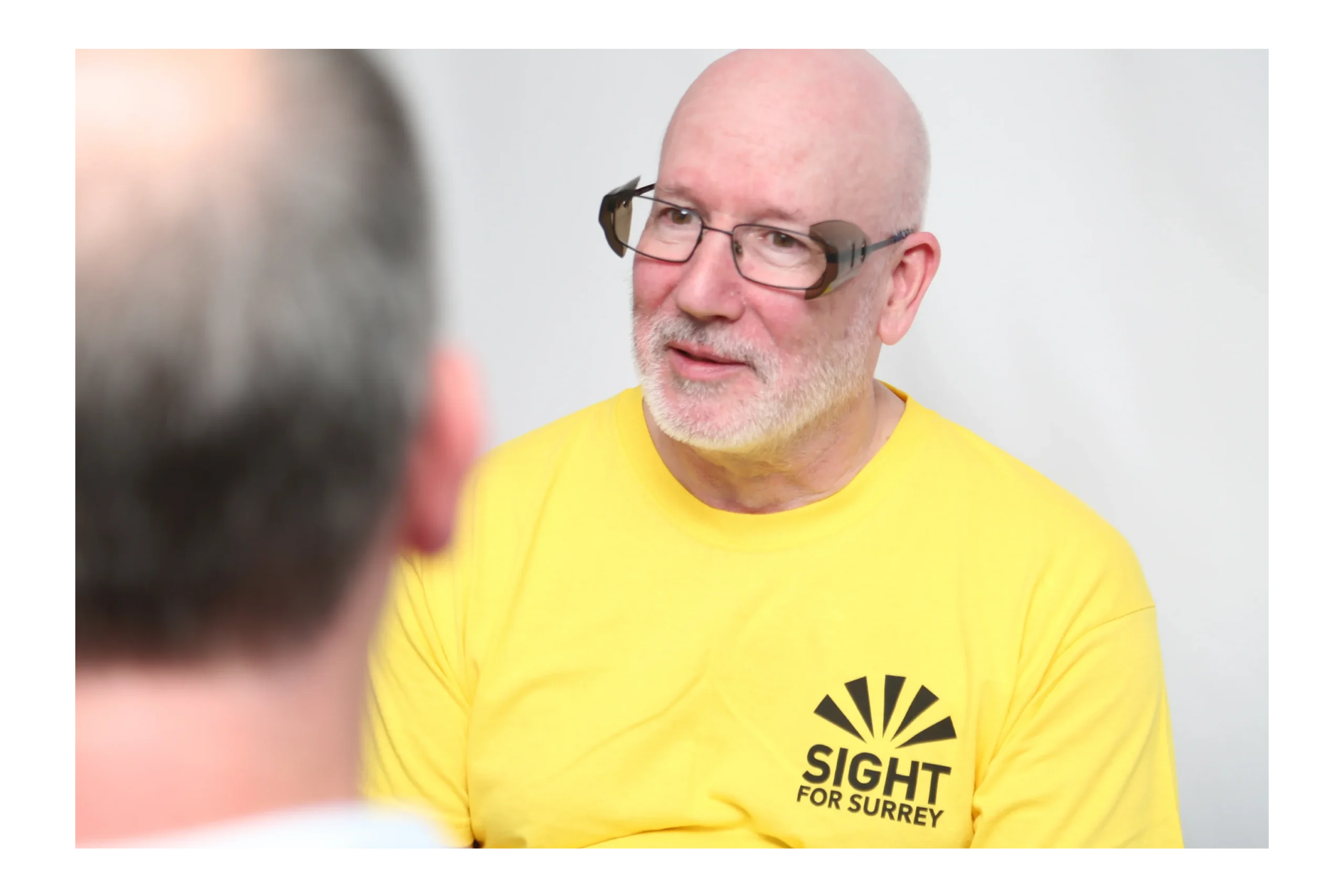 A vision impaired man talking to another person.