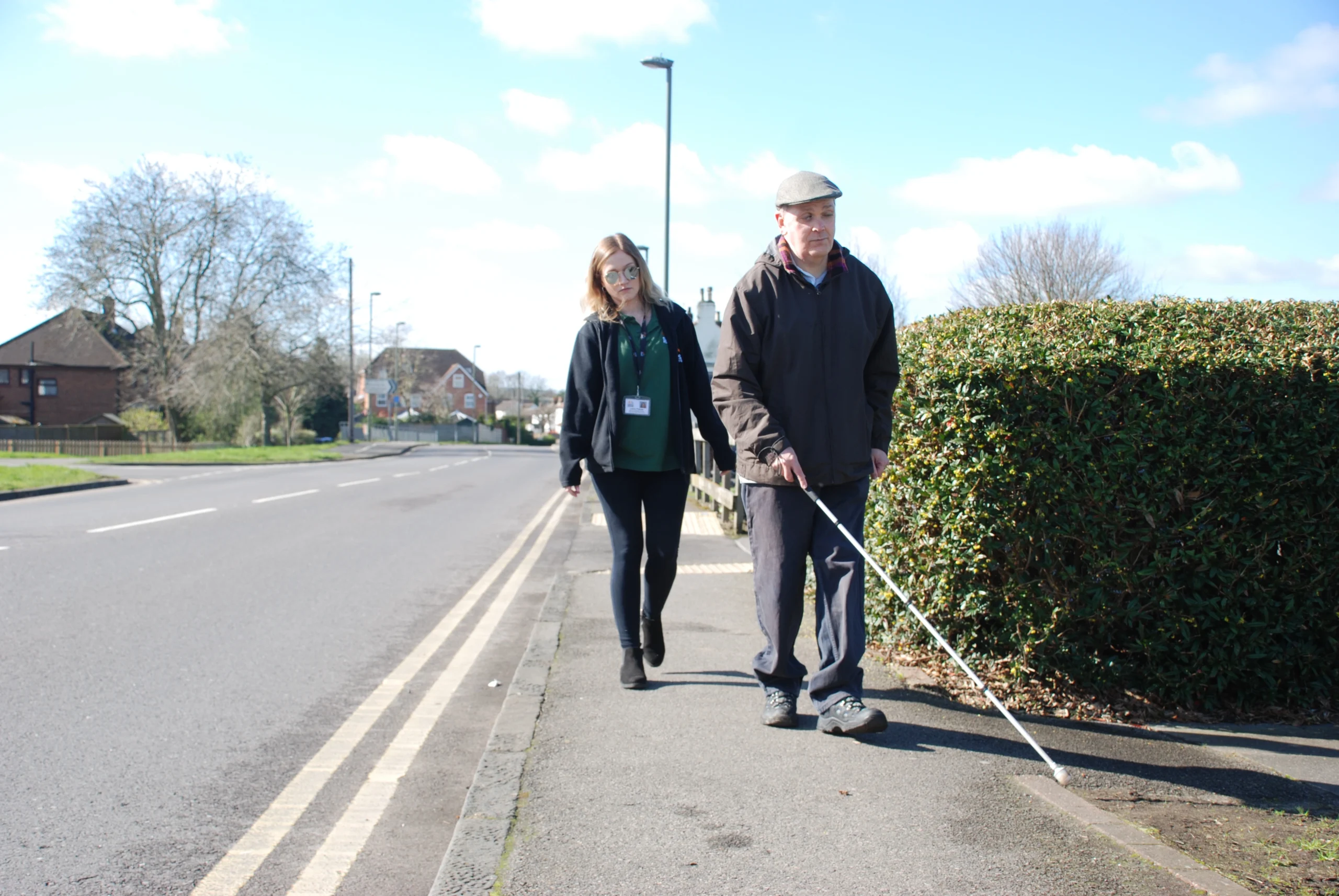 Laura, Rehabilitation Support Worker, doing sighted guided training alongside a road with a man she is supporting with a new route.