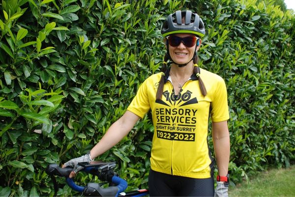 A female cyclist wearing a branded charity t-shirt with one hand on her bike.