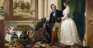 A man and a lady seated and standing in an old room