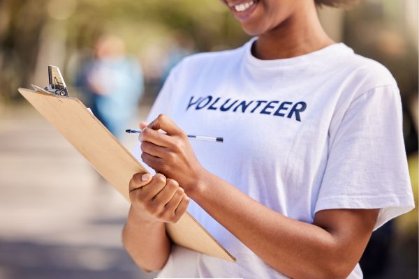A person wearing a t-shirt with the words volunteer printed on it is holding a clip board and pen