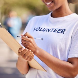 A person wearing a t-shirt with the words VOLUNTEER is holding a clip board and a pen