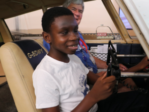 A young boy is sitting in the cockpit of a plane holding the steering wheel.