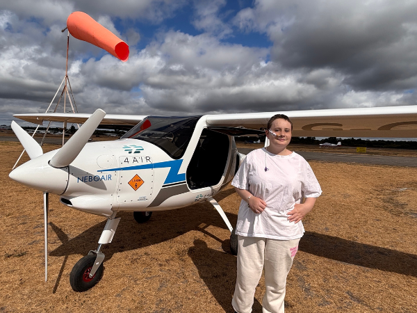 A young person supported by the charity is standing outside a small 2 seater plane.