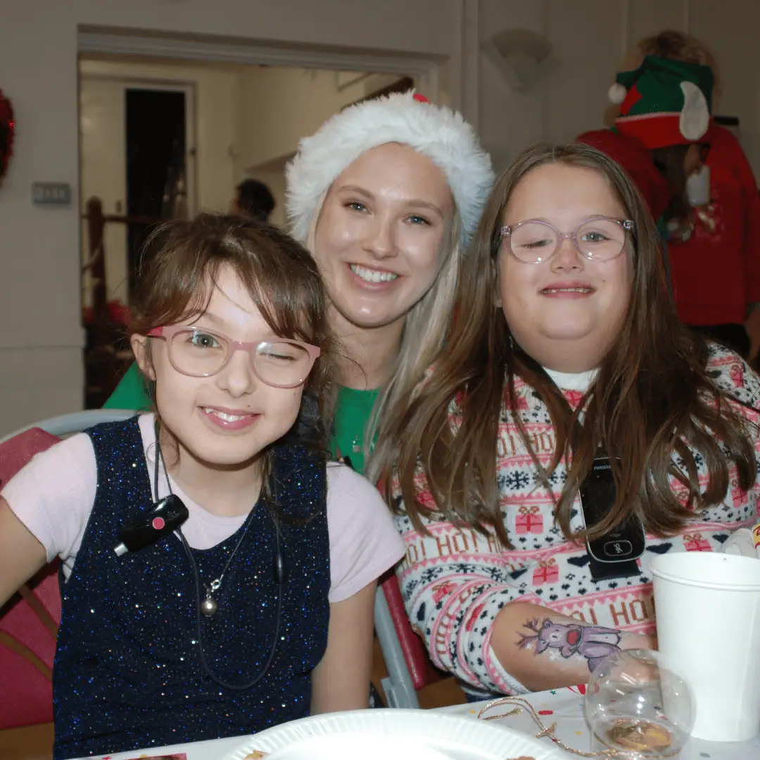 Two girls wearing glasses posing with a women in a Santa hat